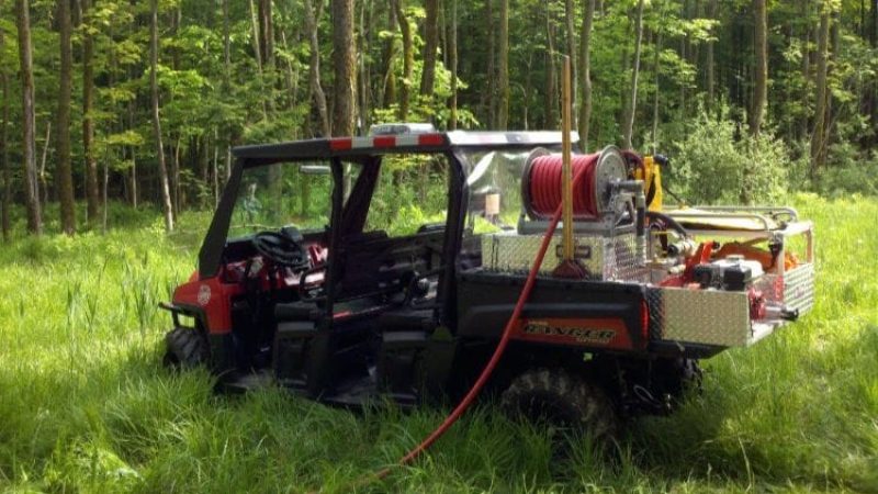 An off-road vehicle in a wooded area. There is a hose in the back of the vehicle.
