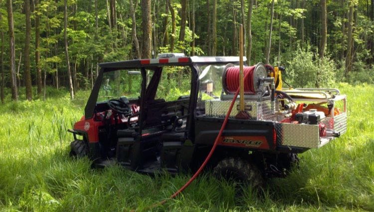 An Off-Road Vehicle In A Wooded Area. There Is A Hose In The Back Of The Vehicle.